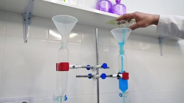 Bilim adamı baraja mavi sıvı boşaltıyor. Sıvı cam tüpe, bebek bezine gidiyor. Araştırmacının eli, emme zamanını kontrol etmek için zamanlayıcıyı tutuyor..