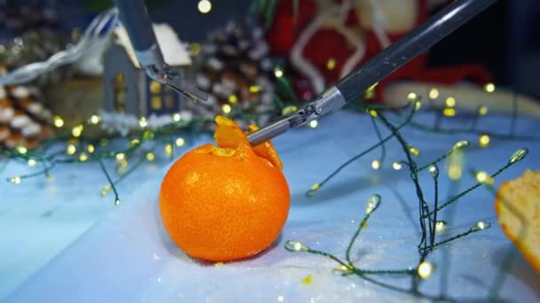 タンジェリンを繊細に皮をむく未来的なロボットアーム 現代手術におけるイノベーション 背景にあるクリスマスの装飾 — ストック動画