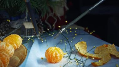 Cerrahi makinenin robot kolları soyulmuş mandalinayı tutar. Üst düzey cerrahi ekipmanlarla soyulmuş meyveler. Arkaplanda Noel süsleri.