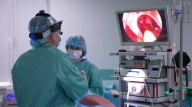 Ameliyathanede ameliyat yapan iki cerrah. Erkek doktor monitöre bakar. Cerrah, yüksek teknolojili ekipmanların yardımıyla ekranda hastanın organlarının durumunu kontrol ediyor..