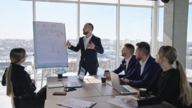 Bir grup iş adamı büyük pencereli bir ofiste toplantı yapıyor. Sunucu, grafiği duygusal ve hareketli bir şekilde tartışıyor. Takım, meslektaşlarını dikkatle dinliyor..