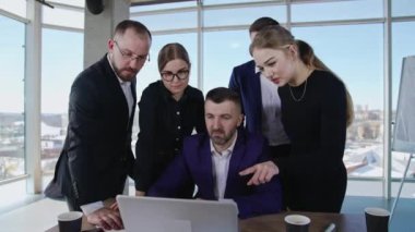 Takım arkadaşları masanın ve dizüstü bilgisayarın etrafında dururlar. Erkekler ve kadınlar bilgisayar ekranında bir şey tartışıyor. Ofisteki iş arkadaşlarının dostça iletişimi..