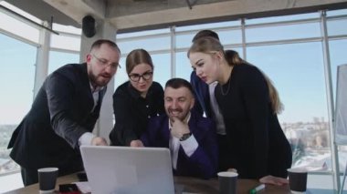 Çalışma ekibi dizüstü bilgisayarın etrafında toplandı, ona baktı, tartıştı ve gülümsedi. Meslektaşlar strateji geliştirir ve önerilerde bulunurlar. Aktif işe katılan ofis ekibi.