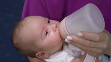 Annesinin ellerinde dinlenen ve biberonla beslenen yeni doğmuş güzel bir çocuk. Küçük çocuk gözlerini kapar ve yavaş yavaş uykuya dalar. Kapat..
