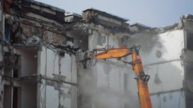 Evi yıkan bir kazıcı makinesinin hidrolik parçalayıcısı. Yüksek bina, özel bir makine tarafından yıkılan bir depremle yıkıldı. Toz her yere yayılıyor..
