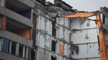 Büyük hidrolik pençeler yıkılan evin beton zeminini kavrıyor. Kazı kazıcı harabe binanın duvarlarını ve zeminini kırmak için yükseğe ulaşır..