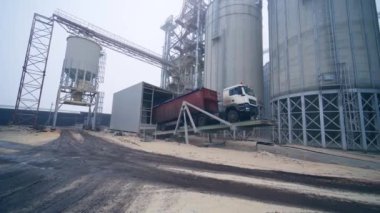 Ürünleri kamyondan tahıl ambarına boşaltıyor. Kamyonet boşaltma sürecini kolaylaştırmak için özel bir platformda duruyor. Asansör fabrikasının arka planında yüklü kamyon..