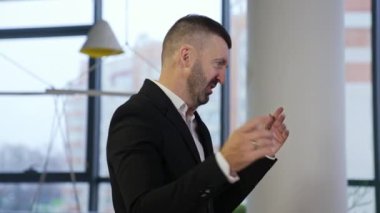 Patron yanında duruyor ve meslektaşlarına bir şeyler söylüyor. Takım elbiseli bir erkek çalışma noktalarını açıklıyor ve elleriyle işaret ediyor. Büyük ofisteki adam..