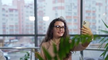 Çekici genç kadın ofiste selfie çekiyor. Kadın çalışan, arkasını dönerken cep telefonuyla video çekiyor..