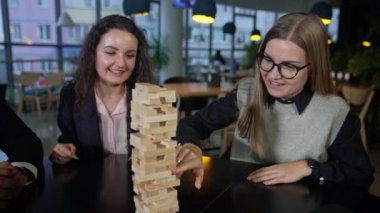 Arkadaşlarla Jenga oynayıp eğleniyoruz. Kızlardan biri, Jenga yığınındaki tuğlayı dikkatlice itiyor. Yetişkinler için boş zaman.