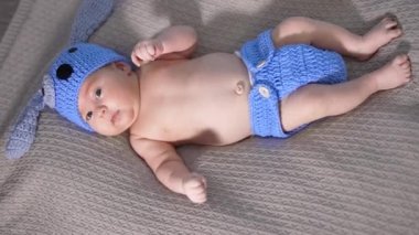 Mavi örgü şapkalı ve bebek bezli küçük bir çocuk sırtüstü yatıyor. Küçük bir bebek için komik bir köpek kostümü. Yukarıdan görüntüle.