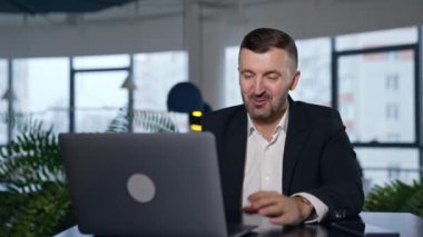 Bilgisayarla iş görüşmesi. İş adamı dizüstü bilgisayarın önünde konuşurken konuşuyor ve gülümsüyor. Arkaplanda bulanık bir ofis.