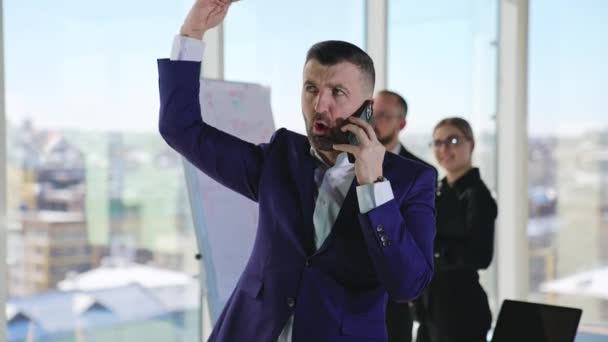 Muž Kanceláři Mluví Telefonu Aktivně Gestikuluje Dva Kancelářští Pracovníci Pozadí — Stock video