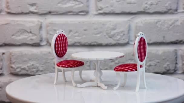 雕刻的木制玩具桌子和两边的两把椅子旋转着 漂亮的家具为洋娃娃的房子 砖墙背景下的白色桌子和红白相间的椅子 — 图库视频影像