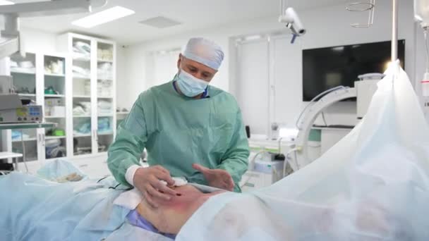 脂肪吸引術の終了について 外科医は 患者が目を覚ます前に仕上げ手順を行っています 医師は患者の腹部をきれいにし 手術をコメントする — ストック動画