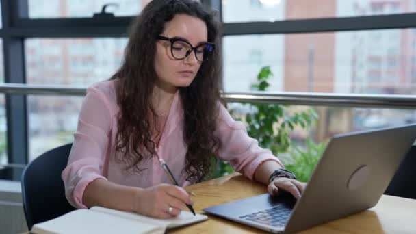 広々としたオフィスでテーブルに座り ノートパソコンで作業し メモを取るビジネスマン コンピュータで情報を探す眼鏡をかけている女性 — ストック動画