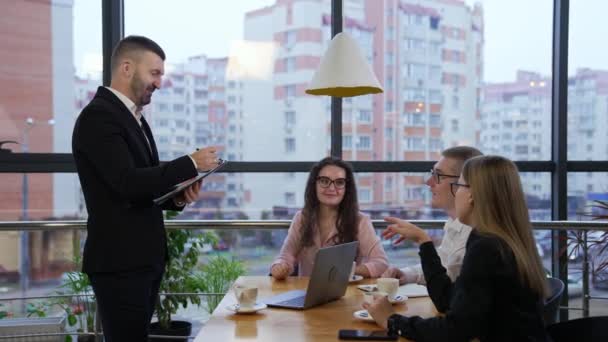 彼の前に座っている同僚と仕事の瞬間を話し合うスーツを着た男 オフィスのコーヒーカップで会話をするワーキングチーム — ストック動画