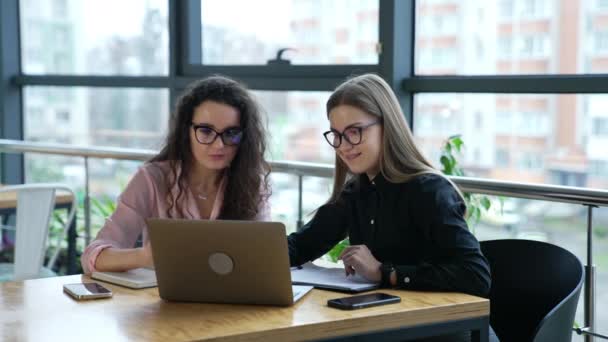 两名女同事在办公室的电脑上讨论了一些事情 戴眼镜的女队员在笔记本电脑前工作 — 图库视频影像