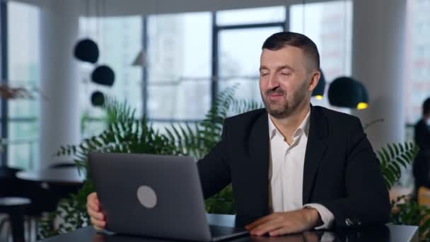 公式のスーツを着たひげ付き男がノートパソコンを開け 会話を始める ビジネス交渉でガジェットを使用する ブラーレッド バックドロップ — ストック動画