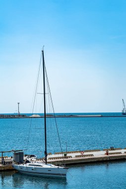 Huzurlu bir yelkenli zarif bir şekilde rıhtımda yüzüyor. Rıhtımın yanındaki suda bir yelkenli.