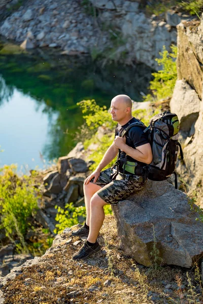 Man Enjoying Serene Nature Moment. A man with a backpack sitting on a rock