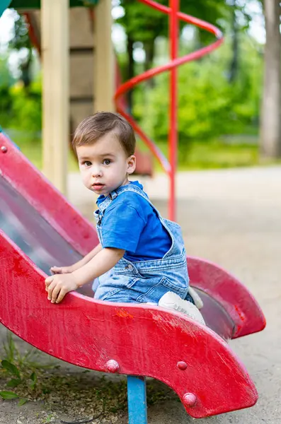 A little boy sitting on a slide in a park