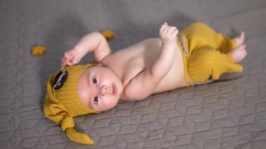 Yatağında düğmesi olan sarı şapkalı bir çocuk. Kollarını ve ayaklarını sallayan komik kostümlü bir bebek. Gri bir geçmişi olan hoş bir çocuk..