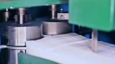 Kalın dönen metal şaftlar gelecekteki bebek bezleri için kumaşları itiyor. Bebek bezleri için dokumasız kumaş yığını. Kapat..