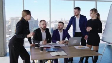 İş arkadaşları masada otururken ya da ayakta sohbet ederken. Ofiste dostane bir iş ortamı var. İş arkadaşları iş yerinde sohbet edip gülümsüyor..
