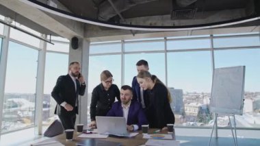 Bir grup iş arkadaşı ellerinde dizüstü bilgisayarla patronun etrafında dikiliyorlar. Diğer işadamlarının telefon görüşmeleri var. Ekip geniş bir ofiste çalışıyor..