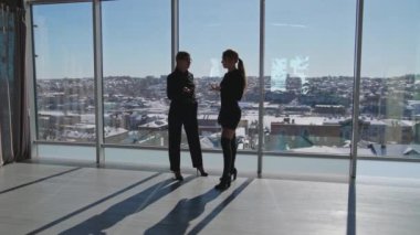 İş yerinde kadınların iletişimi. İki çekici genç kadın pencerede duran bir şeyi tartışıyor. Büyük pencereli güneşli bir ofis..
