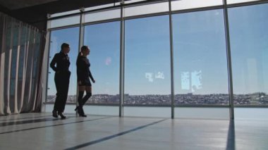 Kadın çalışanlar pencereler boyunca yürür ve konuşurlar. Siyahlı bayanlar pencereden dışarı bakın ve dışarıda bir şey gösterin. Aşağıdan görüntüle.