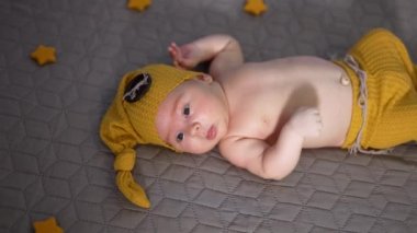 Sarı şapkalı ve pantolonlu şirin bir çocuk. Yatakta çıplak göbekli bir bebek. Çocuğun etrafında küçük oyuncak yıldızlar.