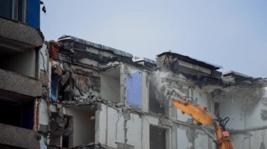 Kazı kazıcı pençesi yıkık binanın parçalarını kırıyor. Düşen molozlarla birlikte tehlikeli bir inşaat alanı. Üst katların yıkılması.