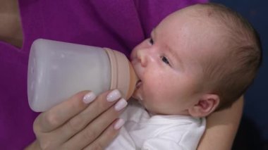 Bebek biberondan yiyor ve biraz süt döküyor. Bakıcı anne bebeğin ağzından ve yanaklarından süt döktü. Kapat..