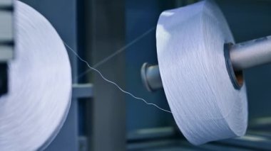 Büyük beyaz iplikler gevşiyor. Bebek bezi üretim tesisinde ağır beyaz iplik makaraları. Kapat..