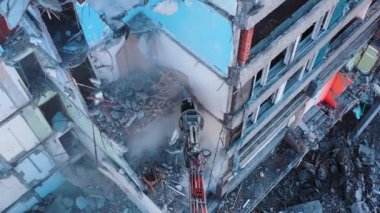 Kazıcı, yıkılan binanın parçalarını koparıyor. Yıkım alanında çalışan ağır makineler. Yukarıdan görüntüle.