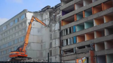 Küçük turuncu yıkım makinesi evi söküyor. Doğa felaketi tarafından yıkılan bir binanın yeniden inşası. Aşağıdan görüntüle.