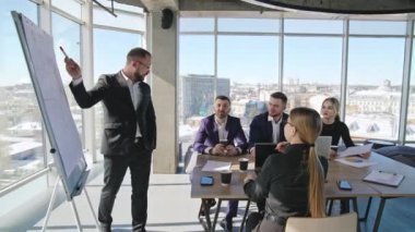 Takım arkadaşları masada oturan stratejileri tartışıyor. İş arkadaşlarının güneşli bir ofiste toplantısı var. Arkaplanda şehir manzarası.