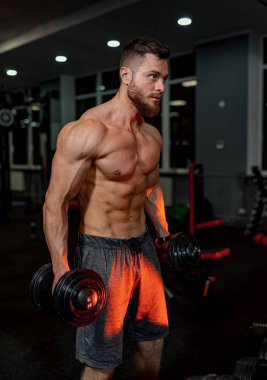 Atletik kasları olan güçlü bir vücut geliştirici. Spor salonunda kaslı üstsüz adam eğitimi..