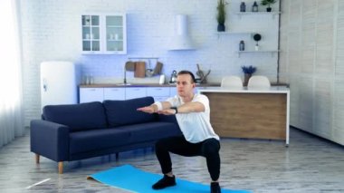 Sporcu evde egzersiz yapıyor. Evdeki oturma odasında çömelme ve egzersiz yapan adam.