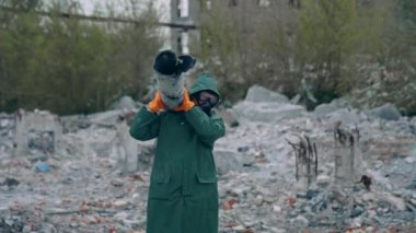 Gaz maskeli bir adam harabeye dönmüş. Koruyucu giysiler ve gaz maskeli bir adam harabe şehirde yürüyor.