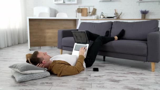 床にラップトップを持っている男 自宅でラップトップを使用して 床に横たわる若者 — ストック動画