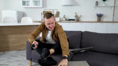 Evdeki kanepede oturan adam. Genç adam evde dinleniyor, çoraplarını fırçalıyor.