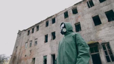 Koruyucu kıyafetli ve gaz maskeli bir çevreci. Gaz maskeli adam neredeyse yıkılmış bir bina.