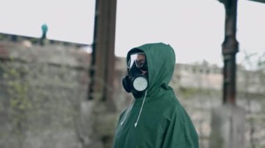 Gaz maskeli ve koruyucu giysili bir adam. Gaz maskeli ve pelerinli bir adam terk edilmiş fabrikada kimyasal koruma için.