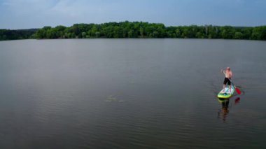 Kürek tahtasında duran adam. Geniş nehirdeki SUP panosunda kürek çeken bir adamın havadan görüntüsü