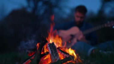 Şenlik ateşinin yanında gitar çalan adam. Şenlik ateşi başında oturan ve akustik gitar çalan yalnız bir adam.