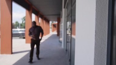 Şehir caddesinde dikilen siyah adam. Arka planda yürüyen takım elbiseli siyah adam.