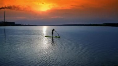 SUP panosunda kürek çeken bir adam. Suyun üzerinde SUP tahtalarıyla dinlenen güzel bir insan manzarası.